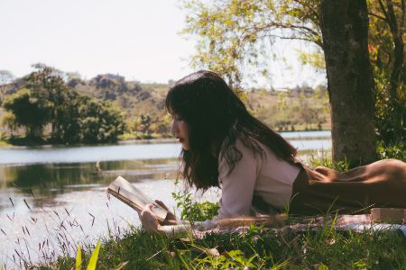 woman reading book by river