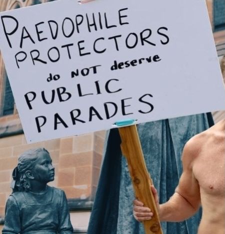 man holding sign saying paedo protectors do not deserve public parades