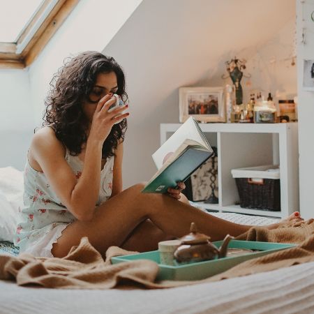woman reading book in bed drinking coffee